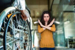 persona su sedia a rotelle e donna che fa no con le braccia